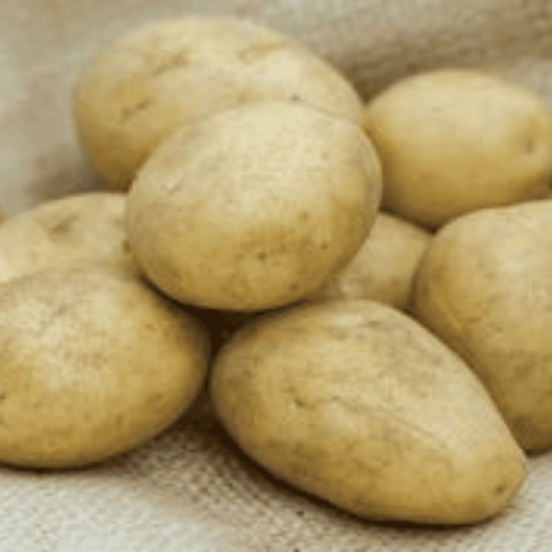 A pile of raw, unpeeled yellow potatoes resting on a textured beige burlap fabric background.